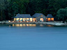 evening sunset of the boathouse from across the water, showing the lights on through it's glass frontend livingroom